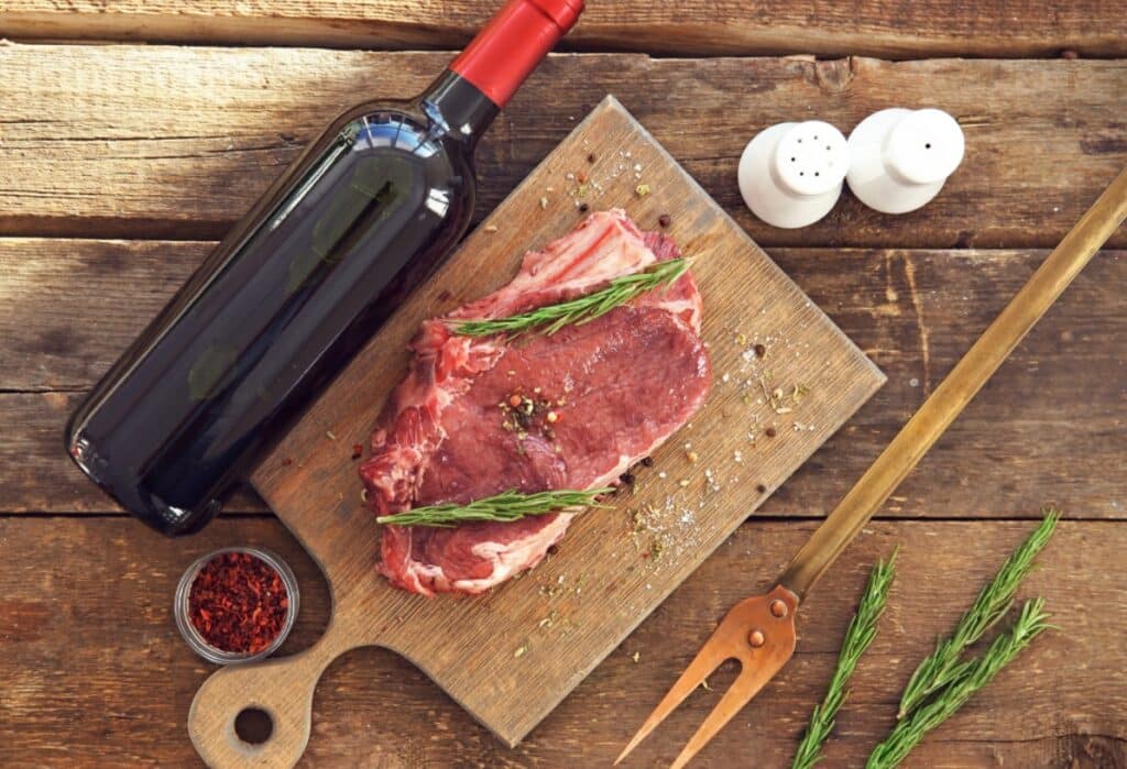 Morceaux de viande avec bouteille de vin et herbes aromatiques