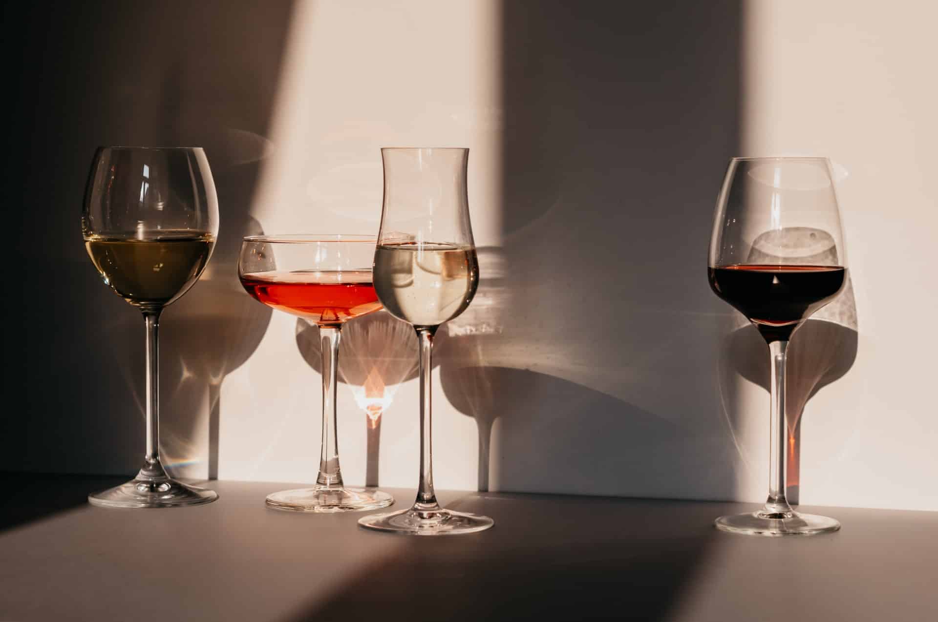 quatre verres de vin blanc rouge rosé contre mur blanc